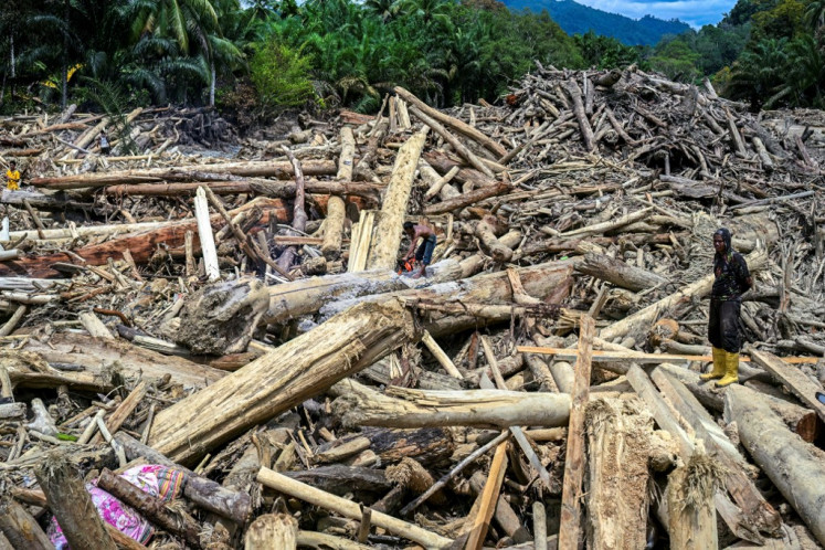 A man stands atop a log amid a pile of wood debris left by floodwaters in North Sumatra&rsquo;s Garoga village on Dec. 4, 2025, as other residents scavenge usable materials to rebuild their damaged homes.
