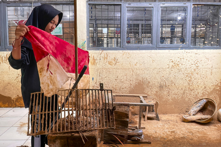 Flood-torn: A student folds a mud-stained Indonesian flag on Dec. 7, 2025, during a clean-up of her flood-affected school in Padang, West Sumatra. Severe floods and landslides killed close to a thousand people on Sumatra in late December 2025.