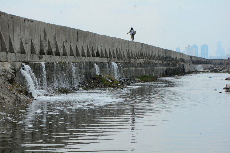 Line of cracks: A man walks with his fishing rod on Dec. 6, 2025, on top of a giant seawall built to prevent flooding, in Muara Baru, North Jakarta. Several sections of the seawall appear to have cracked, allowing seawater to overflow into residential areas.