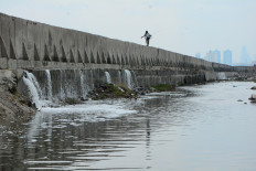 Line of cracks: A man walks with his fishing rod on Dec. 6, 2025, on top of a giant seawall built to prevent flooding, in Muara Baru, North Jakarta. Several sections of the seawall appear to have cracked, allowing seawater to overflow into residential areas.
