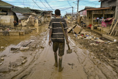 A man with a hoe walks down a street filled with mud and littered with roadside debris on Dec. 6, 2025, after a flash flood hit Aceh Tamiang regency, Aceh.