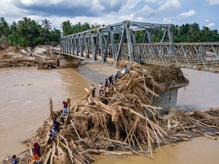 This aerial photo shows people climbing debris, on Dec. 9, 2025, to cross the river on a newly built bridge, connecting Aceh and North Sumatra province, after being destroyed by flash floods along Peusangan river in Bireuen district, Aceh.