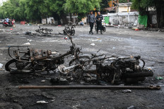 People walk past a burned motorcycle on Dec. 12, 2025, following unrest in the Kalibata area of South Jakarta. Nine kiosks, six motorcycles and one car were set on fire by a mob, allegedly triggered by the assault of two debt collectors on Jl. Raya Kalibata a day earlier.
