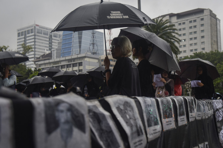 Human rights activist and Kamisan (Thursday) silent protest initiator Maria Catarina Sumarsih (center) stands under an umbrella on Dec. 4, 2025, during a rally near Merdeka Palace in Central Jakarta. During the 889th edition of the Kamisan protests, activists demand several points, including the cessation of criminalizing human rights defender, and the fair resolution of past human rights violations.