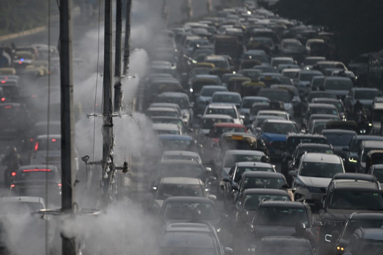 Commuters drive past as anti-smog sprinklers on lamp posts spray water to curb air pollution in New Delhi on December 9, 2025. 