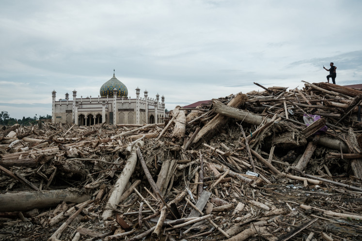 Flood aftermath: A man takes pictures on Dec. 13 as he stands on piles of uprooted trees swept away by a flash flood at Darul Mukhlisin Islamic boarding school in Aceh Tamiang, Aceh. Devastating floods and landslides have killed 1,006 people in Indonesia, rescuers said on Dec. 13 as the nation grapples with the huge scale of relief efforts.