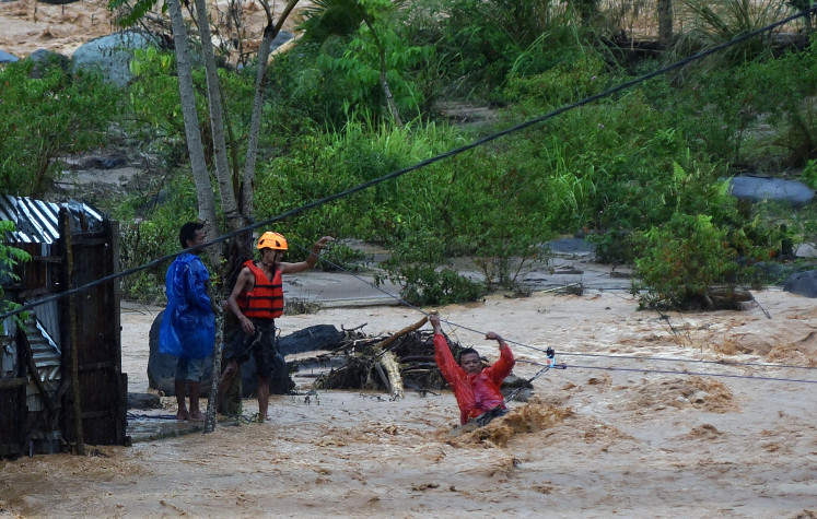 Search and rescue team members guide residents as they cross floodwaters using a rope in the Batu Busuak area in Padang, West Sumatra, on Dec. 14, 2025.