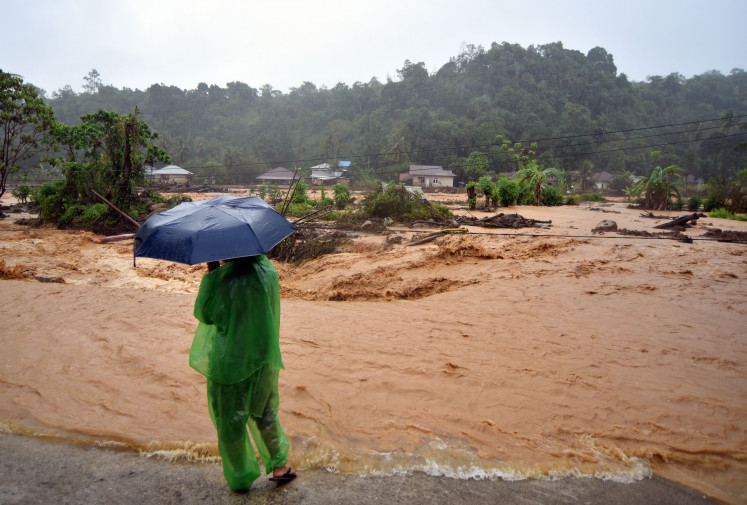 A person watches as river water overflows onto a road on Dec. 14 in the Batu Busuk area of Pauh, Padang, West Sumatra. River water in the flash flood-affected residential area overflowed again, forcing the evacuation of several residents to safer locations.