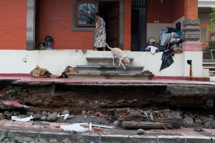 A woman stands by the collapsed wall of her house on Dec. 16, 2025, after flooding in Batuan village, Gianyar, Bali. Flooding triggered by heavy rain in the tourist area on Monday also damaged a motorcycle and a car and injured one person.