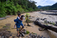 A man holding a child crosses a river on Dec. 16 after floodwaters washed out a road in Batu Busuak, Pauh, Padang, West Sumatra. 