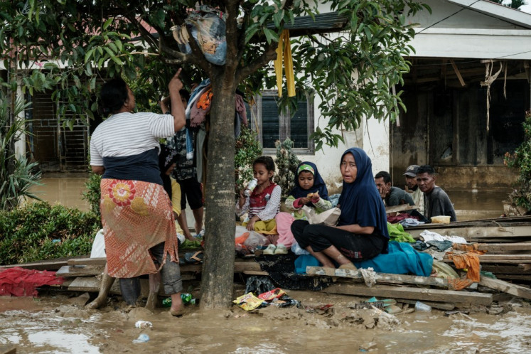 People gather under a tree to shelter from the rain following a flash flood about three weeks ago in Aceh Tamiang, Northern Sumatra, on December 16, 2025. 