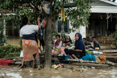 People gather under a tree to shelter from the rain following a flash flood about three weeks ago in Aceh Tamiang, Northern Sumatra, on December 16, 2025. 