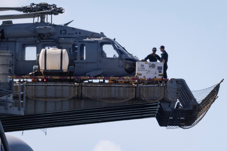 Personnel are seen next to a US Navy MH-60S Knighthawk helicopter sited on the flight deck of the amphibious assault ship USS Iwo Jima (LHD-7) while the vessel is docked in Ponce amid ongoing military movements in Puerto Rico, December 17, 2025. 
