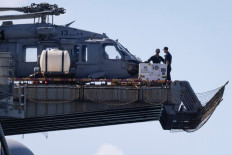 Personnel are seen next to a US Navy MH-60S Knighthawk helicopter sited on the flight deck of the amphibious assault ship USS Iwo Jima (LHD-7) while the vessel is docked in Ponce amid ongoing military movements in Puerto Rico, December 17, 2025. 