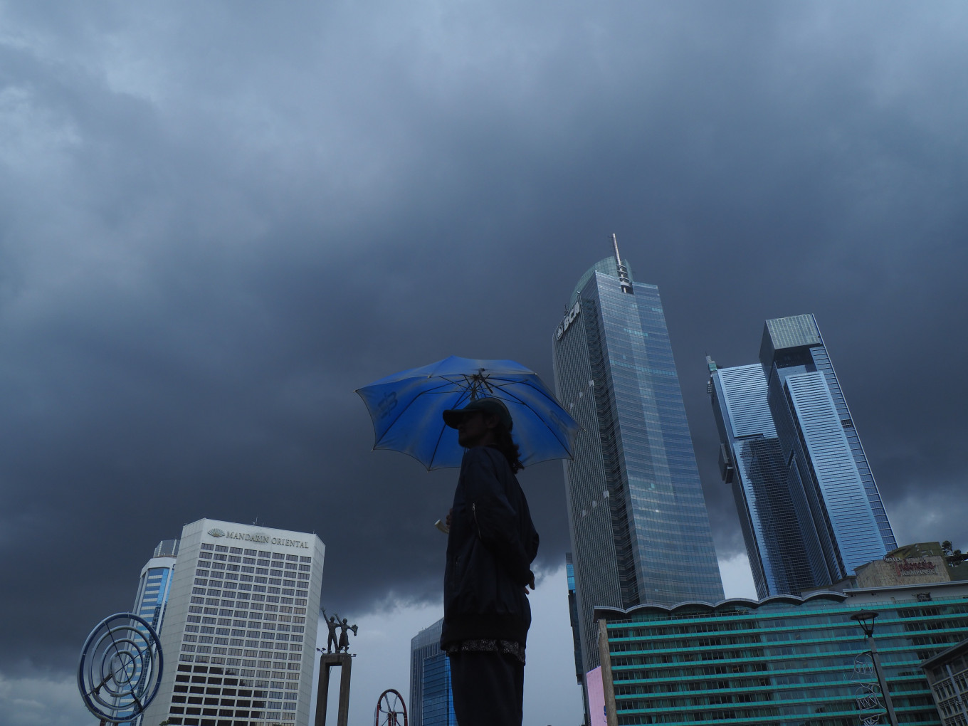 A man holds an umbrella under overcast skies near the Hotel Indonesia traffic circle in Central Jakarta, on Friday, Dec. 19, 2025. Jakarta is stepping up disaster mitigation, with heavy rains and strong winds forecast during the year-end holidays.