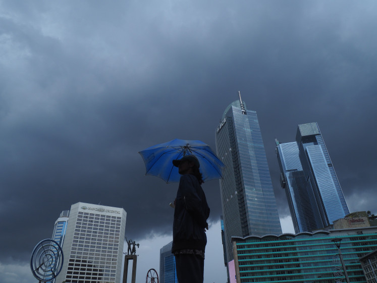 A man holds an umbrella under overcast skies near the Hotel Indonesia traffic circle in Central Jakarta, on Friday, Dec. 19, 2025. Jakarta is stepping up disaster mitigation, with heavy rains and strong winds forecast during the year-end holidays.