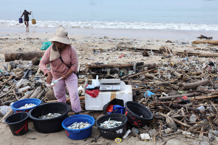 Never-ending: A fish vendor stands near trash on Dec. 19, 2025, during an emergency cleanup at Kedonganan Beach, Badung, Bali. The trash is swept on to the beach by the sea and originates from various area across the resort island.