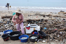 Never-ending: A fish vendor stands near trash on Dec. 19, 2025, during an emergency cleanup at Kedonganan Beach, Badung, Bali. The trash is swept on to the beach by the sea and originates from various area across the resort island.