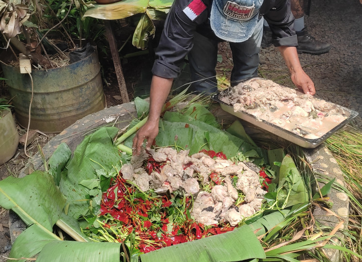 Hot stones: Papuan chef Charles Toto arranges chicken over vegetables coated in buah merah, a deep-red Papuan fruit, before covering them with leaves and cooking the dish using the bubigi stone-cooking technique on Dec. 10, 2025, at Javara Culture Garden Store, in Bekasi, West Java.