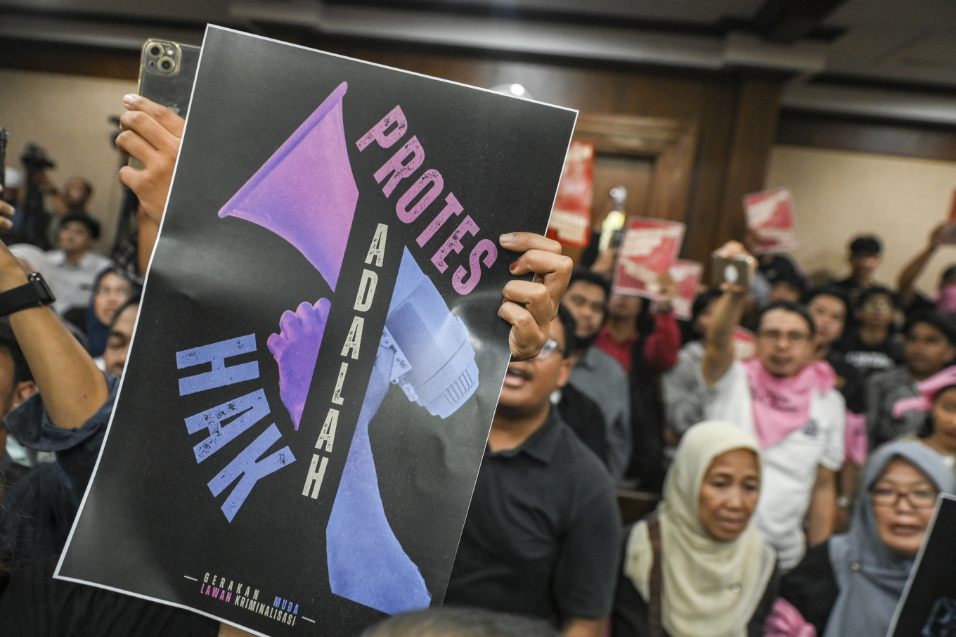 People hold up posters that read &ldquo;Protes adalah hak&ldquo; (Protest is a right) ahead of the indictment hearing on Dec. 16, 2025, against Delpedro Marhein, executive director of rights group Lokataru Foundation, at the Central Jakarta District Court. Prosecutors indicted Delpedro for allegedly inciting hostility toward the government and encouraging students, including minors, to take part in riots.