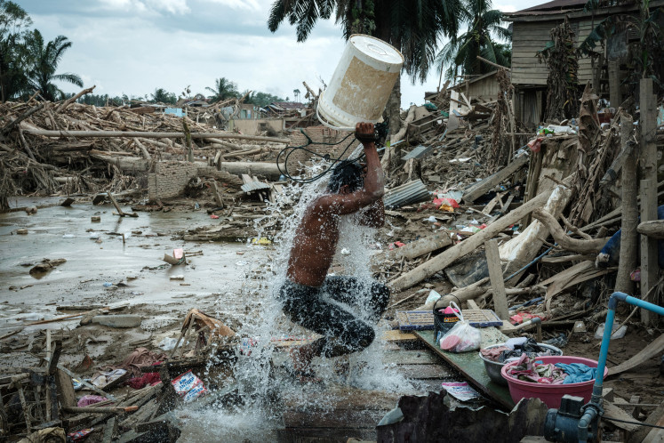 A man uses a bucket to wash off mud on Dec. 13, in Aceh Tamiang, Aceh, surrounded by the devastation wrought by flash flooding and landslides that swept through three provinces in northern Sumatra. 