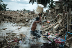 A man uses a bucket to wash off mud on Dec. 13, in Aceh Tamiang, Aceh, surrounded by the devastation wrought by flash flooding and landslides that swept through three provinces in northern Sumatra. 