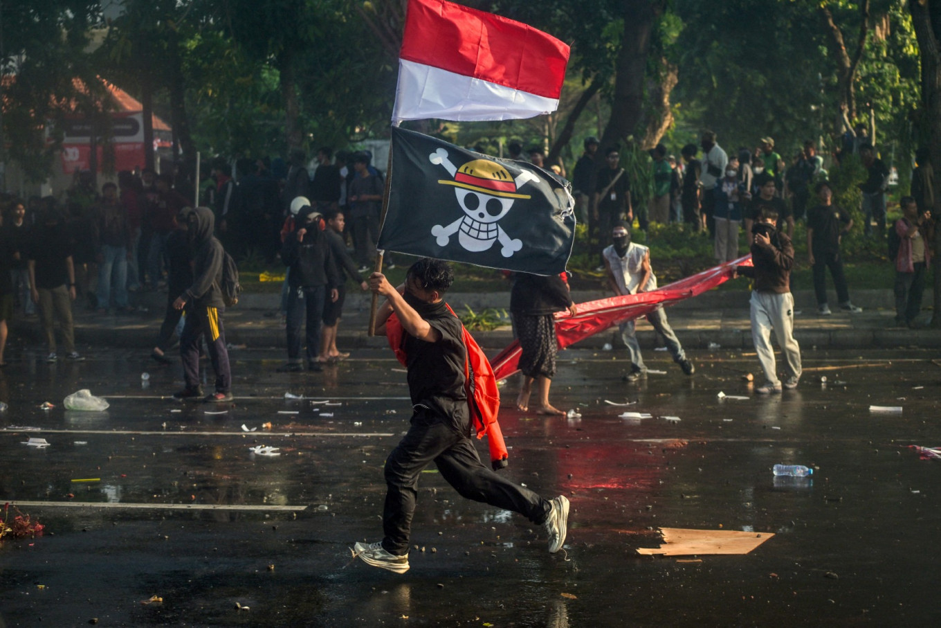 A demonstrator carries the Red-and-White National Flag and a pirate flag from Japanese anime 'One Piece' during a protest in front of the East Java gubernatorial residence in Surabaya, East Java on Aug. 29, 2025, against police brutality after the killing of an 'ojol' (online motorcycle transportation) driver in Jakarta  motorbike taxi driver the previous night. Clashes between protesters and police broke out on Aug. 28 over calls for higher wages and perceived lavish perks for lawmakers, as public discontent grows over the government's handling of the economy.
