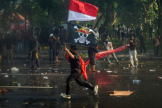 A demonstrator carries the Red-and-White National Flag and a pirate flag from Japanese anime 'One Piece' during a protest in front of the East Java gubernatorial residence in Surabaya, East Java on Aug. 29, 2025, against police brutality after the killing of an 'ojol' (online motorcycle transportation) driver in Jakarta  motorbike taxi driver the previous night. Clashes between protesters and police broke out on Aug. 28 over calls for higher wages and perceived lavish perks for lawmakers, as public discontent grows over the government's handling of the economy.