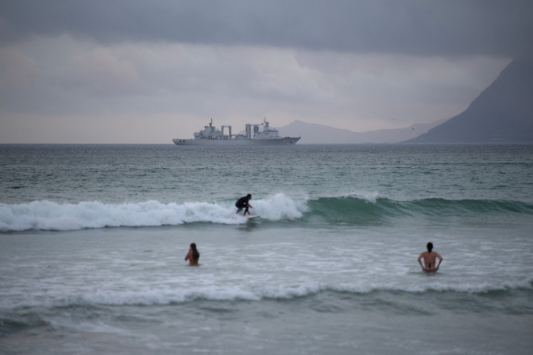 A surfer rides a wave with the Chinese comprehensive supply ship Taihu (Hull 889) in the background in False Bay, close to Simon's Town, near Cape Town, on January 6, 2026. 