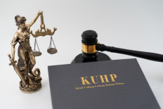 Illustration of a Criminal Code (KUHP) book next to a gavel and a Lady Justice statue.