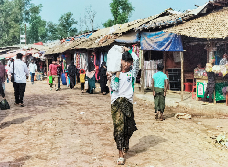 Precarious living: A Rohingya refugee carrying a sack walks across a market on Jan. 12 at the Kutupalong refugee camp in Ukhia, Bangladesh.