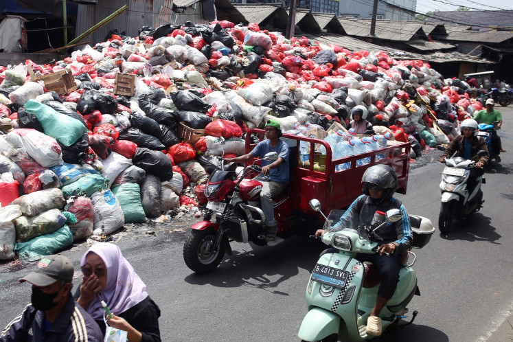 Motorists pass a pile of household waste on Jan. 6 in South Tangerang, Banten. The municipality administration has declared a waste emergency due to unmanaged waste generated across the city in the past month.