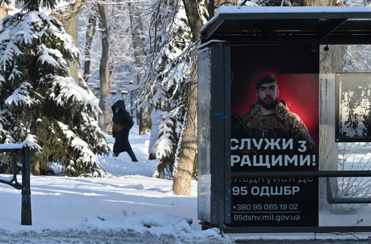 A woman walks behind a bus stop displaying a Ukrainian army recruiting placard on Jan. 16 in Kyiv, amid the Russian invasion of Ukraine.