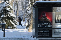 A woman walks behind a bus stop displaying a Ukrainian army recruiting placard on Jan. 16 in Kyiv, amid the Russian invasion of Ukraine.