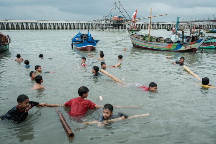 Children play in the water, using bamboo pieces as floats on September 20, 2025, next to a seawall in Cilincing, North Jakarta.
