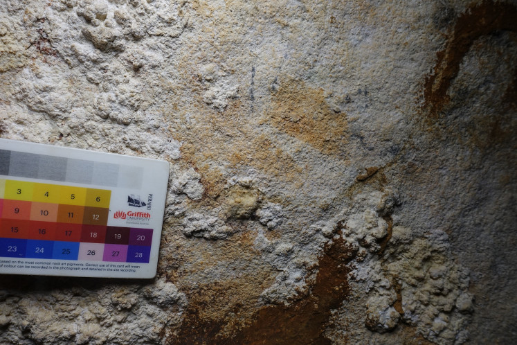 The faded hand stencil that is dated at least 67,800 years old is pointed by a color palette chart held by the archaeologist during an expedition at the Liang Metanduno cave on Muna Island, Southeast Sulawesi in May 2019.