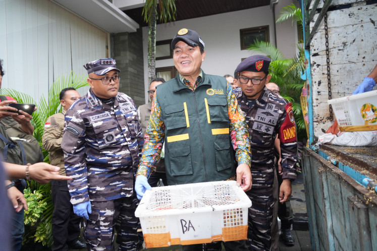 Indonesian Quarantine Agency (Barantin) head Sahat M. Panggabean (center) is flanked by Denpasar Naval Base commander Col. Cokorda GP Pemayun (left) and Karangasem Naval Post commander First Lt. I Ketut Yasa, while carrying a basket of birds during a press conference on Jan. 21 in Padangbai, Karangasem, Bali. The birds were smuggled onboard a truck crossing from neighboring Lombok Island, West Nusa Tenggara, without proper documents. 
