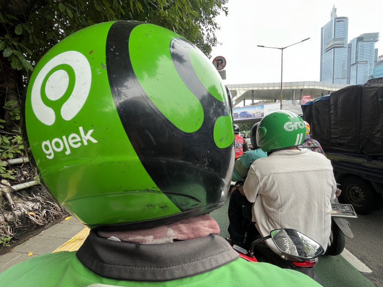 The logos of ride-hailing service providers Gojek and Grab are seen on helmets worn by an online motorcycle taxi driver and another passenger in Jakarta on Jan. 26, 2026.