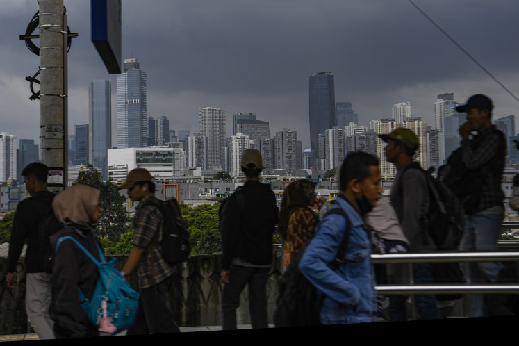 Commuters look on as dark clouds on Jan. 23, 2026 hang over high-rise buildings in Jakarta