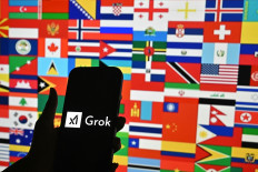 Grok-ing the future: A person holds a smartphone bearing the logo of Grok, a generative artificial intelligence chatbot developed by United States company xAI in front of the national flags of various countries on Jan. 15, 2026, in Bengaluru, India. 