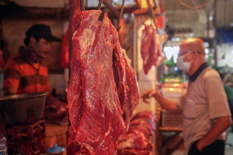 A fresh cut of beef hangs on a hook as a meat vendor (left) attends to a customer on April 6, 2021, at Cijantung Market in East Jakarta. 