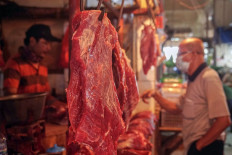 A fresh cut of beef hangs on a hook as a meat vendor (left) attends to a customer on April 6, 2021, at Cijantung Market in East Jakarta. 