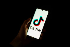 This photograph taken on April 19, 2024, shows a man holding a smartphone displaying the logo of Chinese social media platform Tiktok in an office in Paris. 