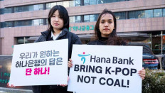 Lee Da-yeon (left) and Nurul Sarifah of Kpop4planet, a global K-pop fans forum, hold signs demanding that Hana Bank cease funding nickel projects on Feb. 2, 2026.