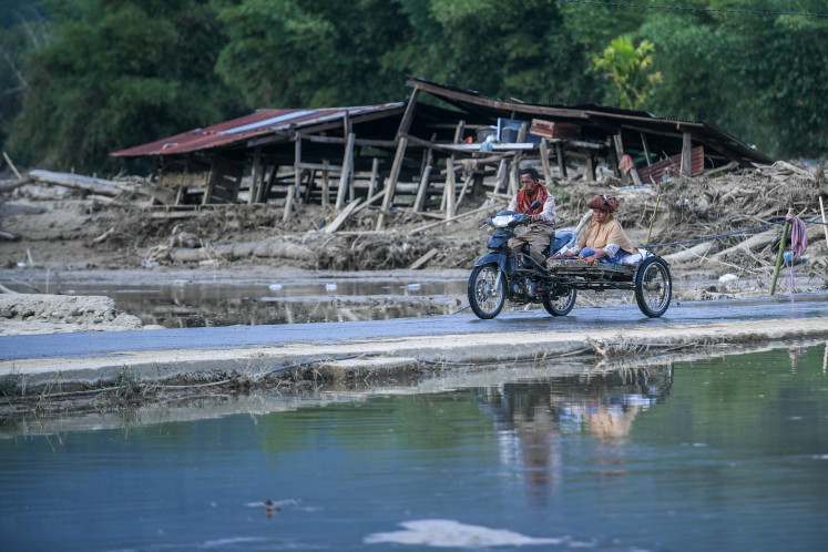 People ride past a destroyed house on Feb. 1, 2026, after flash floods in Kuta Lintang village, Blangkejeren district, Gayo Lues regency, Aceh. 