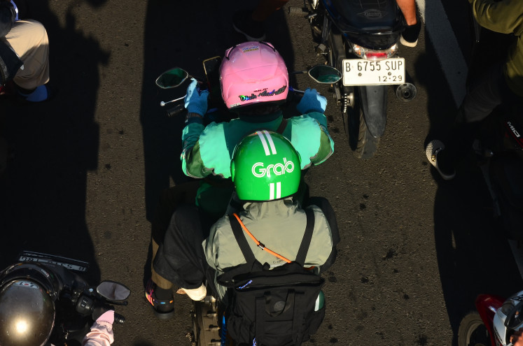 Slow move: Logos of ride-hailing service providers &ldquo;Grab&rdquo; is seen on helmets worn by an online motorcycle taxi passenger in Jakarta on Feb. 4.