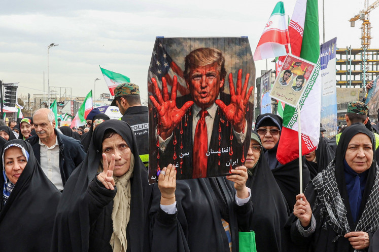 Demonstrators march with a sign depicting United States President Donald Trump with bloodied hands during a rally in Tehran on Feb. 11, 2026, to mark the 47th anniversary of the 1979 Islamic revolution.