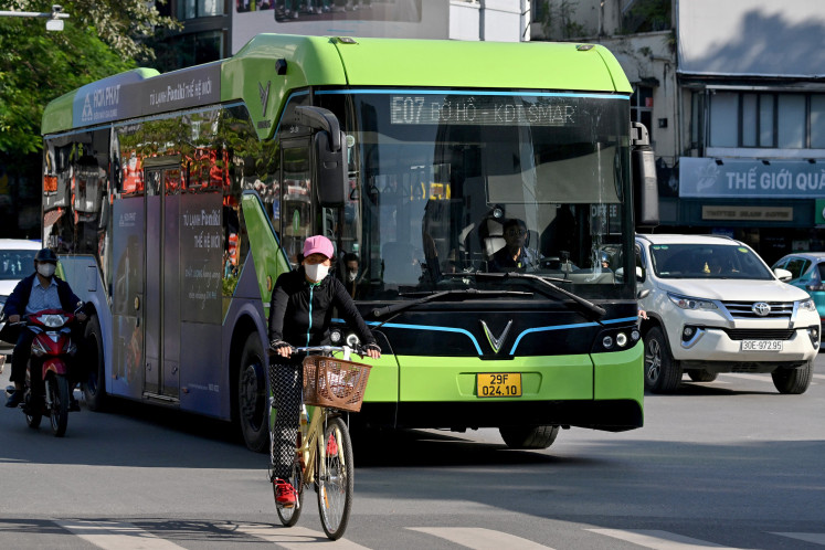 A woman rides a bicycle in front of an electric bus on the street in Hanoi on Nov. 21, 2025.
