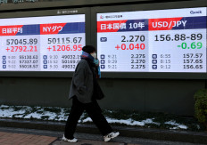 A woman walks past an electronic board displaying the Nikkei share average, the Dow Jones Industrial Average, the level of Japan's 10-year government bonds and the exchange rate between the US dollar and Japanese yen, outside a brokerage in Tokyo on Feb. 9, 2026.