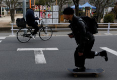 A man on a skateboard crosses a street as a cyclist rides past election campaign posters for the Feb. 8 snap election, displayed on a board in Tokyo on Feb. 6, 2026.